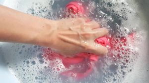 Female hand wash a pink T-shirt in a basin