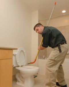 Plumber unclogging a toilet with manual auger