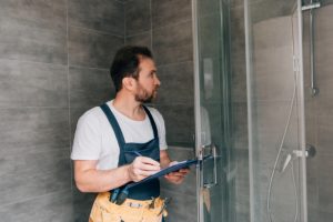 adult male plumber making notes in clipboard while checking shower in bathroom
