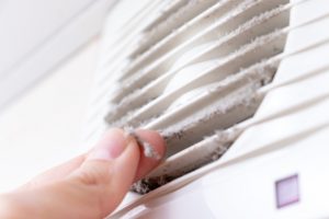 dusty white plastic ventilation air grille and a hand holding dust by fingers