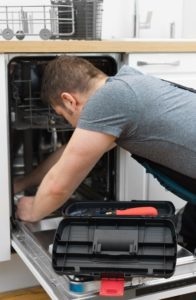 Professional handyman repairing dishwasher in the kitchen