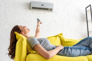 young woman relaxing under air conditioner and holding remote control