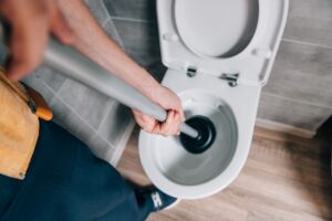 male plumber using plunger and cleaning toilet in bathroom