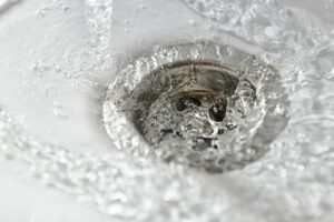 stream of clean water flows into the drain hole of a white sink