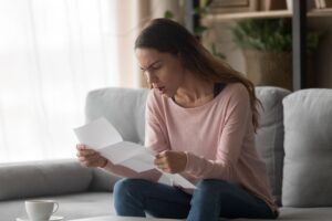 Angry woman sitting on couch holding letter reading awful news