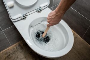 cropped view of plumber using plunger in toilet bowl during flushing in modern restroom with grey tile