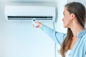 Young attractive woman using remote controller for adjustment air conditioner temperature in room at home.