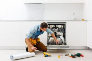 Technician sitting near dishwasher with screwdriver in kitchen with instruments