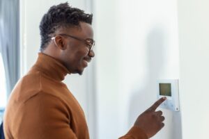 Smiling African American man using modern smart home system, controller on wall