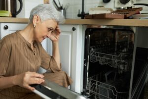 Frustrated woman trying to fix her dishwasher at home